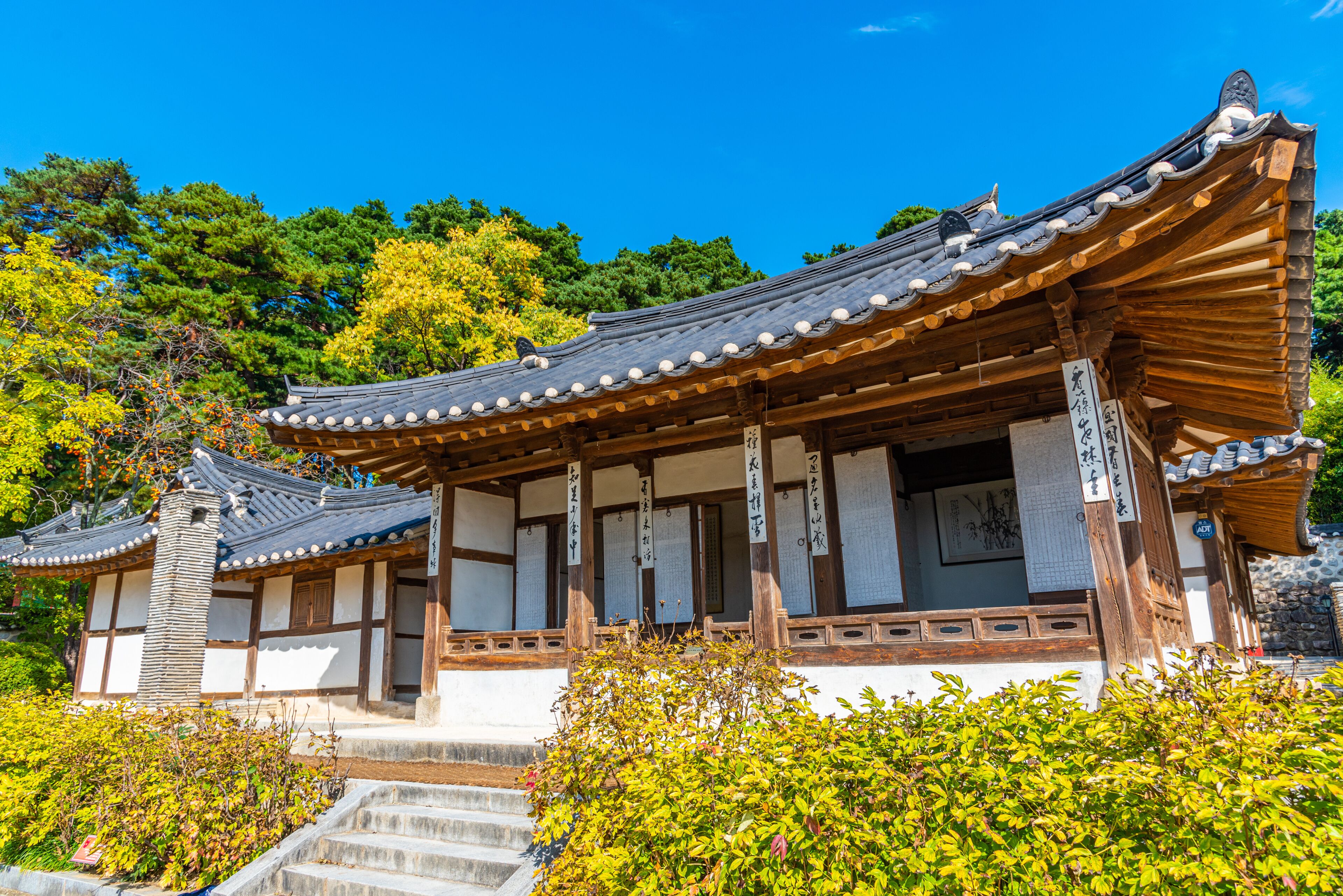 A traditional Japanese building with a tiled roof and wooden beams, surrounded by lush greenery and trees.