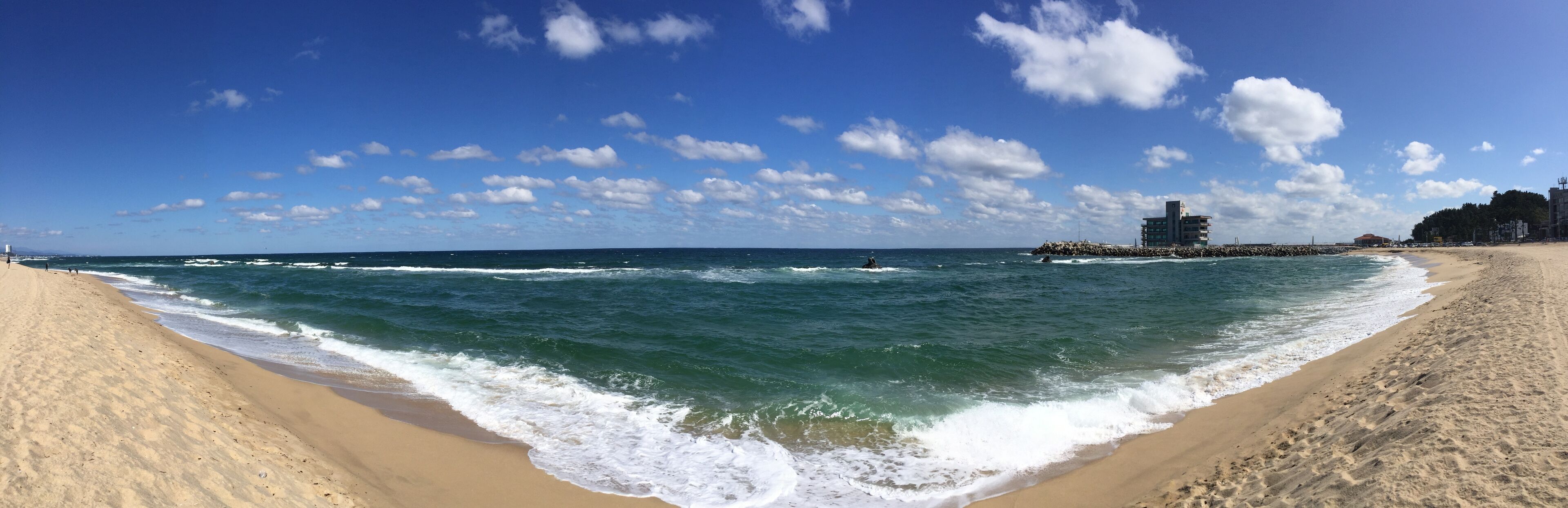 A beach with waves, a pier, and buildings in the background.