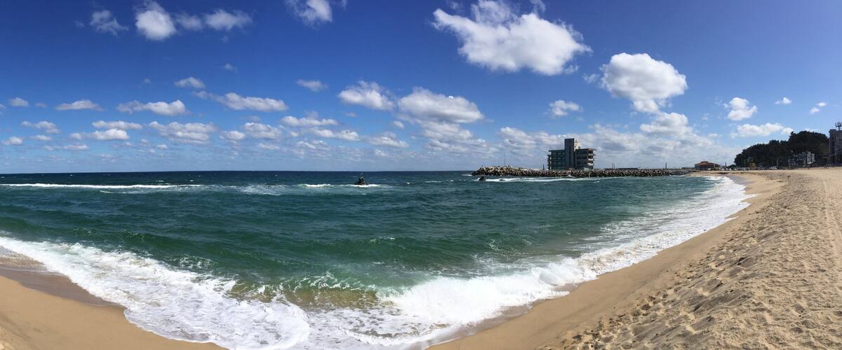 A beach with waves, a pier, and buildings in the background.