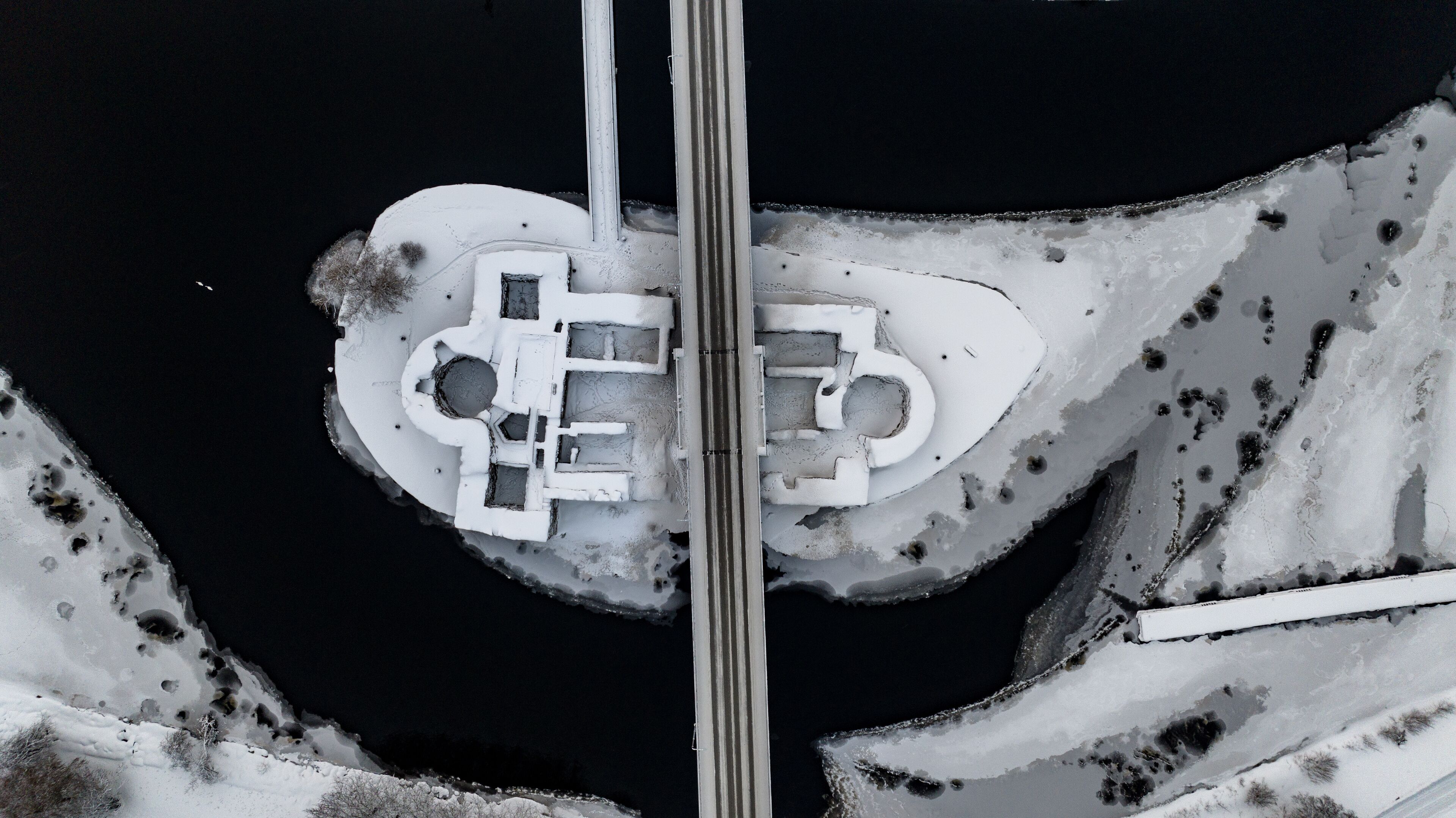 Aerial view of the snow-dusted Kajaani Castle ruins embraced by dark, icy waters under a stark winter sky, Kajaani, Kainuu, Finland.