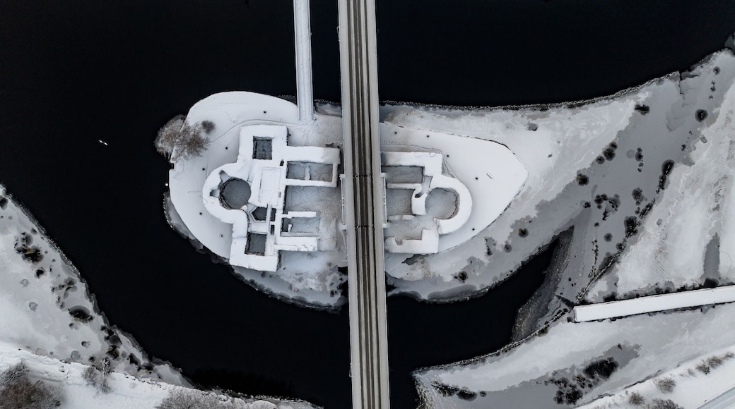 Aerial view of the snow-dusted Kajaani Castle ruins embraced by dark, icy waters under a stark winter sky, Kajaani, Kainuu, Finland.
