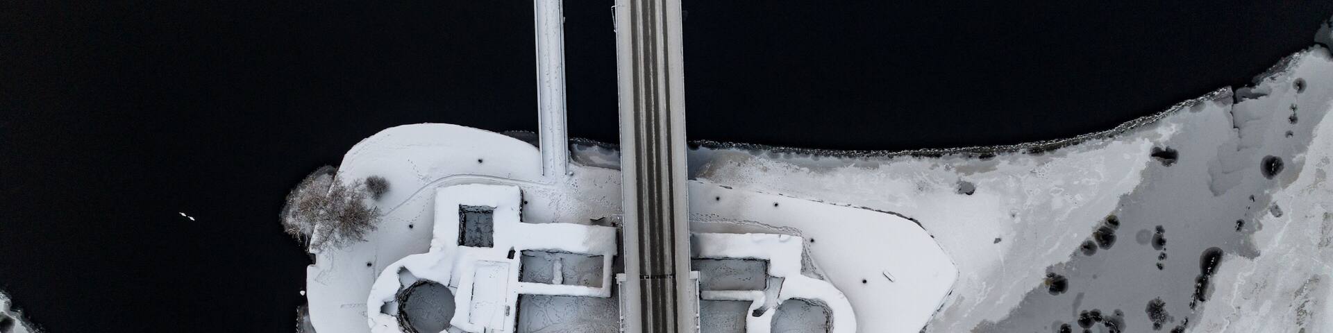 Aerial view of the snow-dusted Kajaani Castle ruins embraced by dark, icy waters under a stark winter sky, Kajaani, Kainuu, Finland.