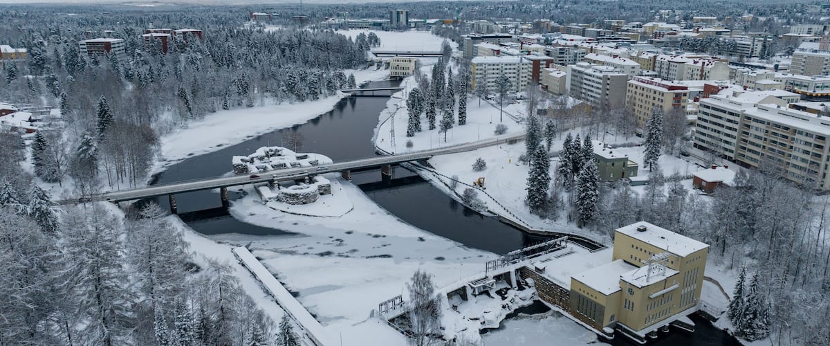 Een met sneeuw bedekte stadsgezicht met een rivier, een brug en omliggende bomen.