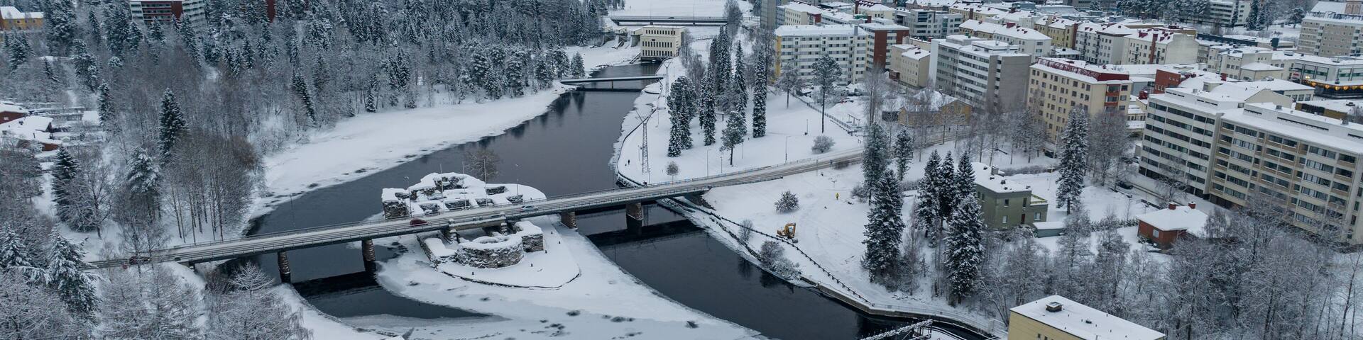 A snow-covered cityscape with a river, a bridge, and surrounding trees.