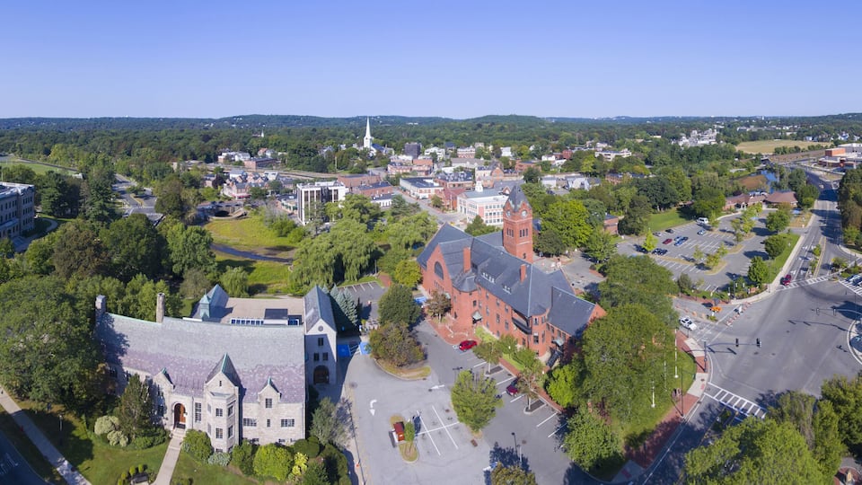 A town with a prominent church, a large building with a clock tower, and a mix of residential and commercial buildings surrounded by greenery.