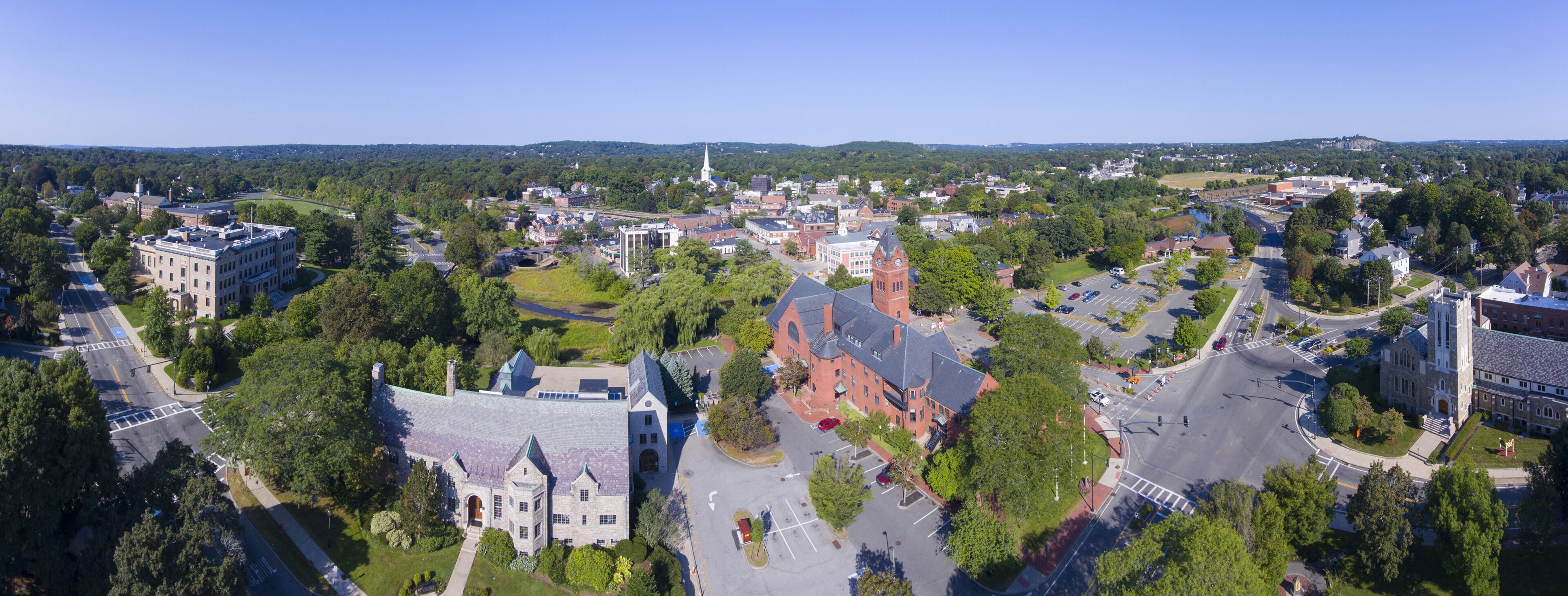 A town with a prominent church, a large building with a clock tower, and a mix of residential and commercial buildings surrounded by greenery.