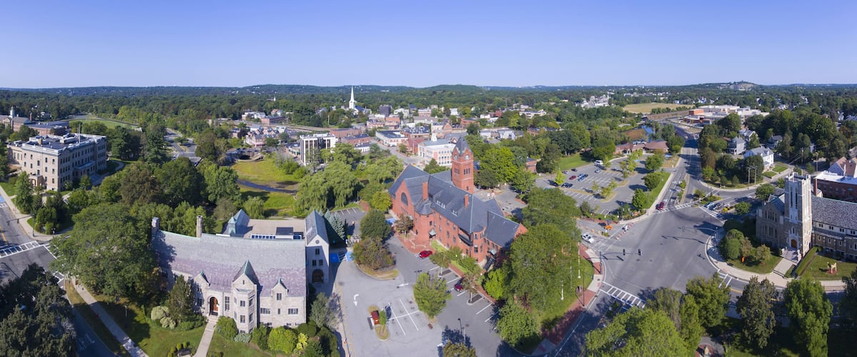 A town with a prominent church, a large building with a clock tower, and a mix of residential and commercial buildings surrounded by greenery.