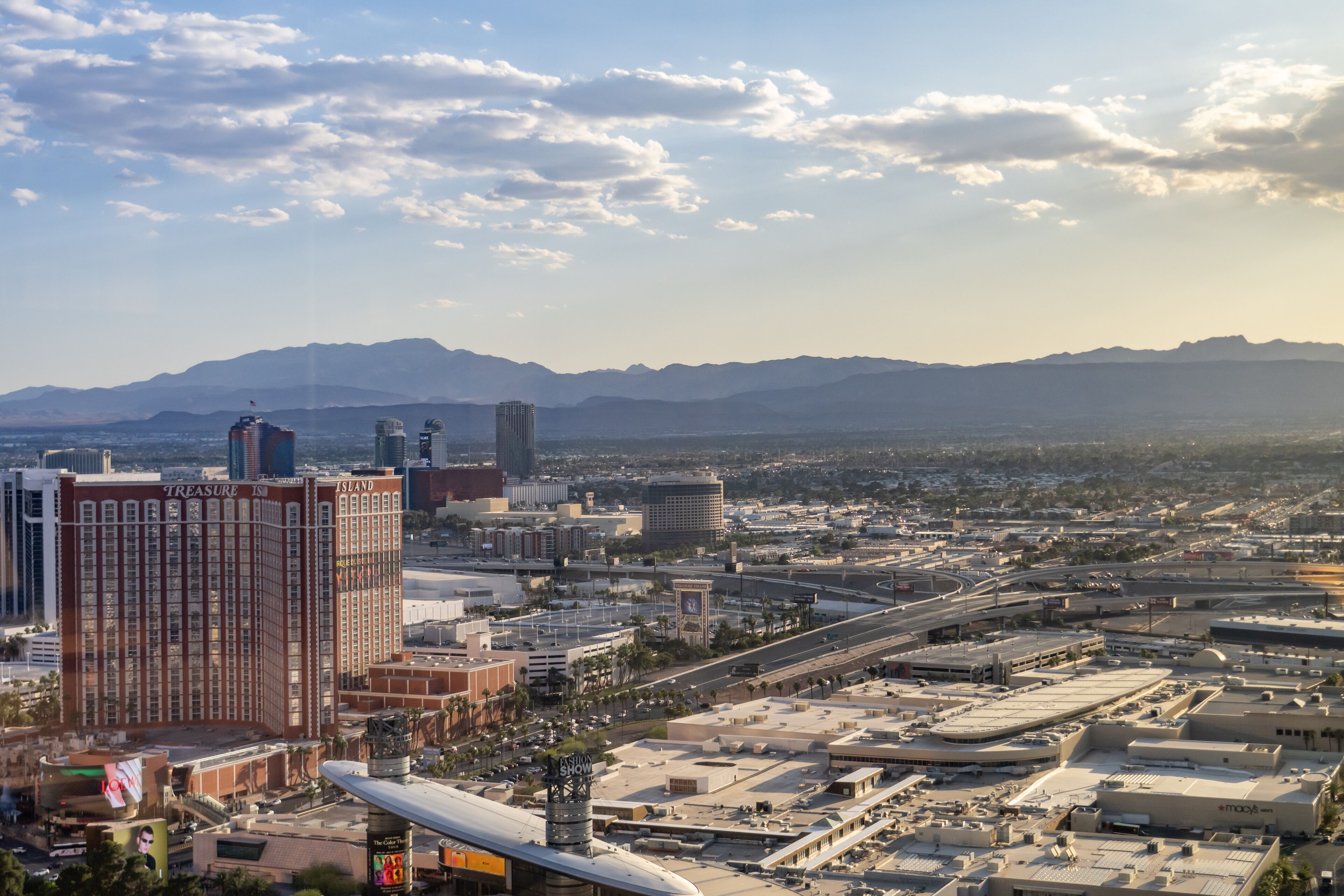 A cityscape with prominent buildings like 'Treasure Island' and 'Island' hotel, a highway, and distant mountains.