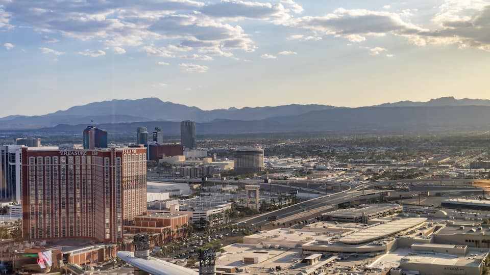 A cityscape with prominent buildings like 'Treasure Island' and 'Island' hotel, a highway, and distant mountains.