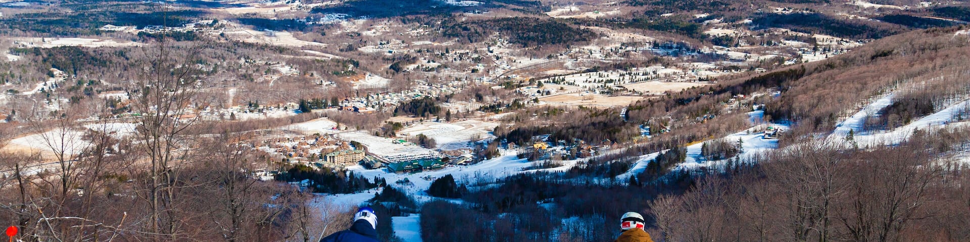 Two skiers on a snowy slope with a valley and mountains in the background.