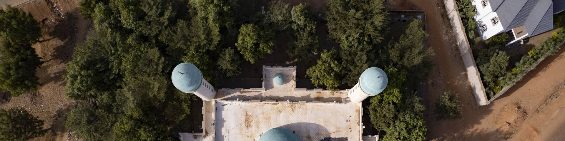Aerial view of an elegant mosque, its turquoise domes contrasting with the surrounding verdant trees and the arid landscape, Gabasawa, Kano, Nigeria.