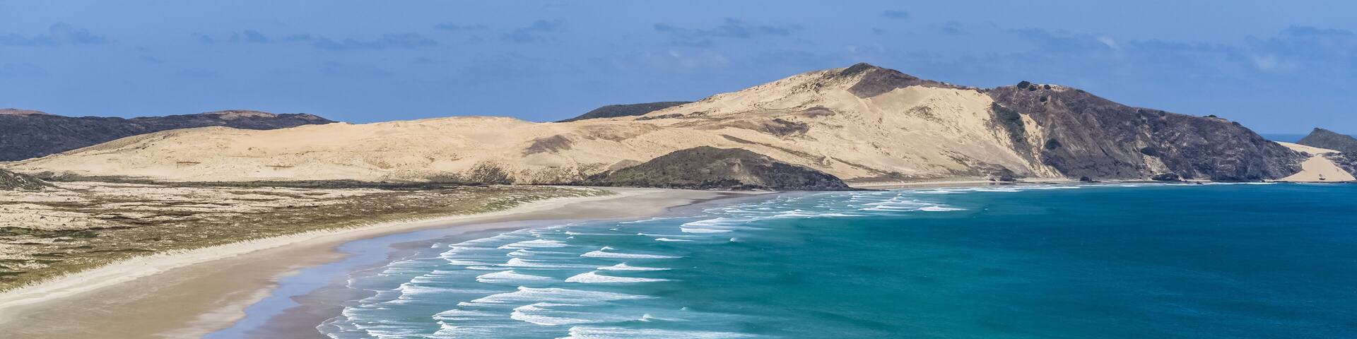 A beach with turquoise waves and a mountainous backdrop.