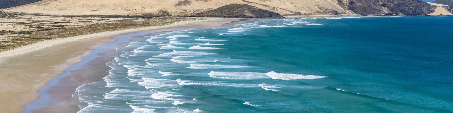 Una playa con olas turquesas y montañas al fondo.