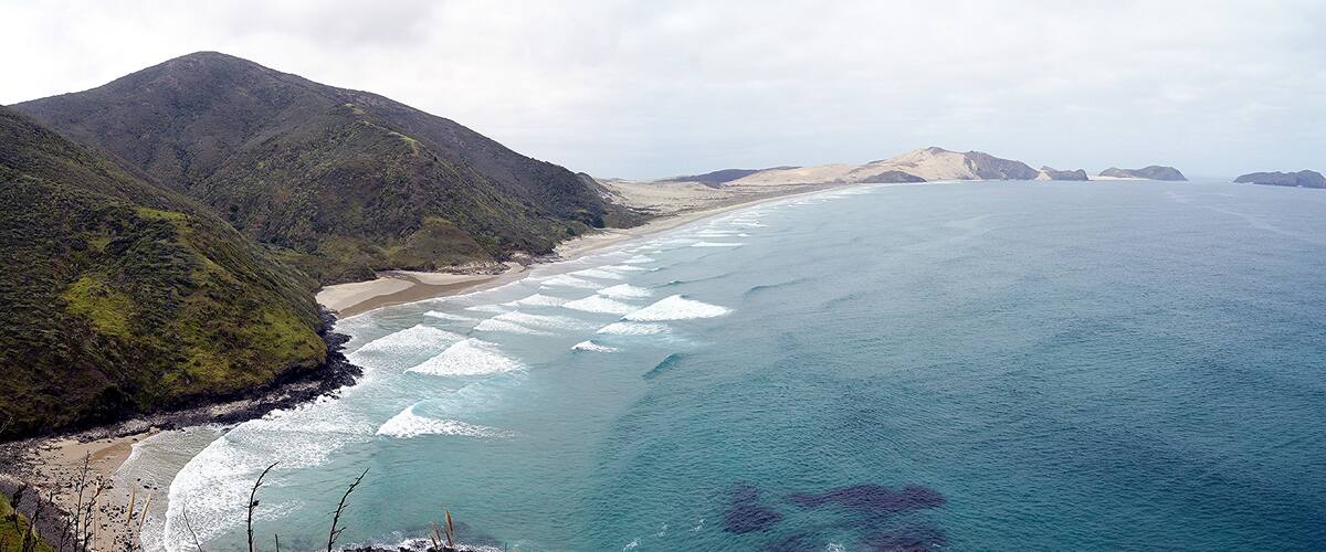 A coastal landscape with a sandy beach, turquoise waters, and green hills.