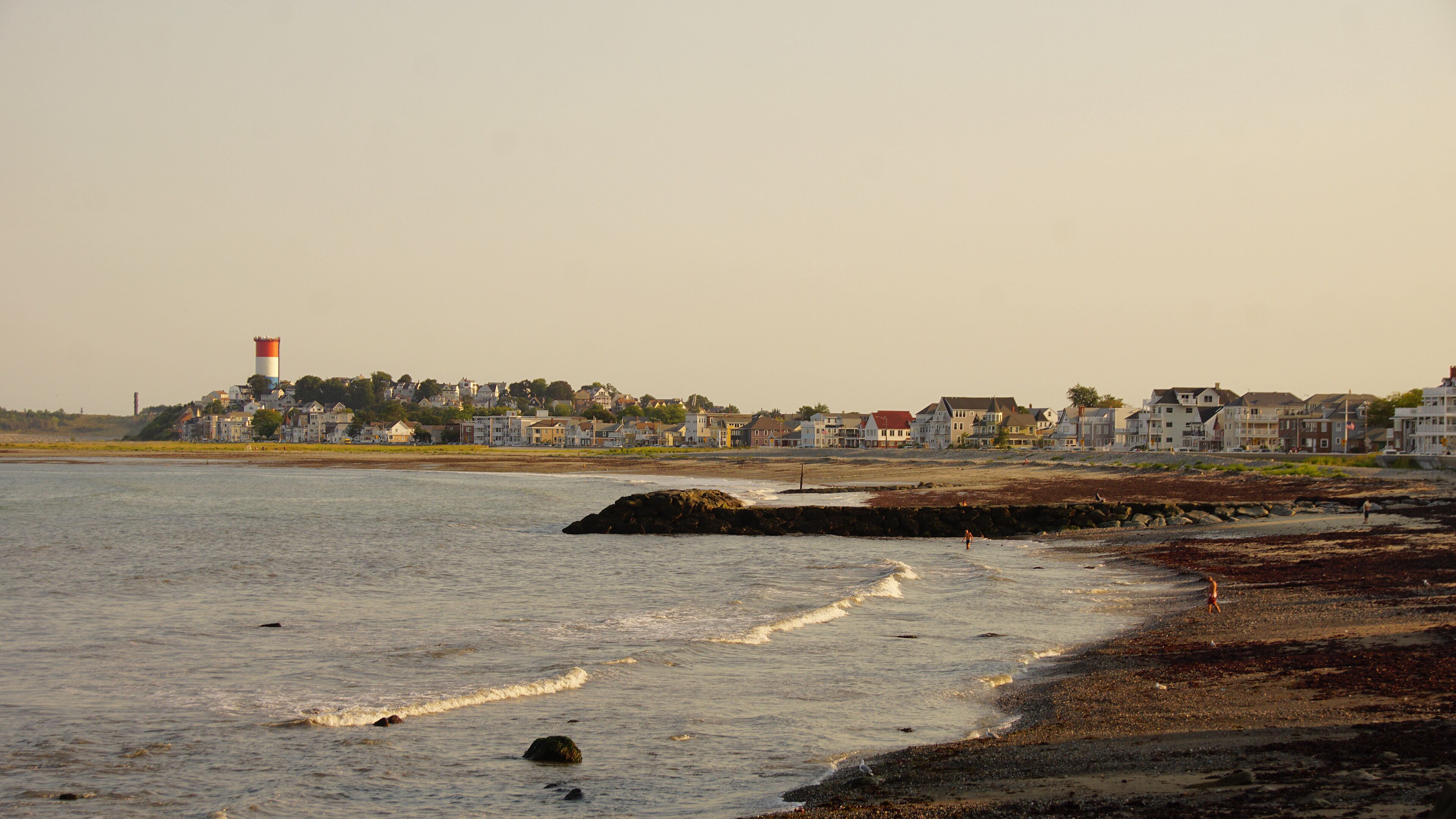 A coastal town with a lighthouse, sandy beach, and residential buildings.