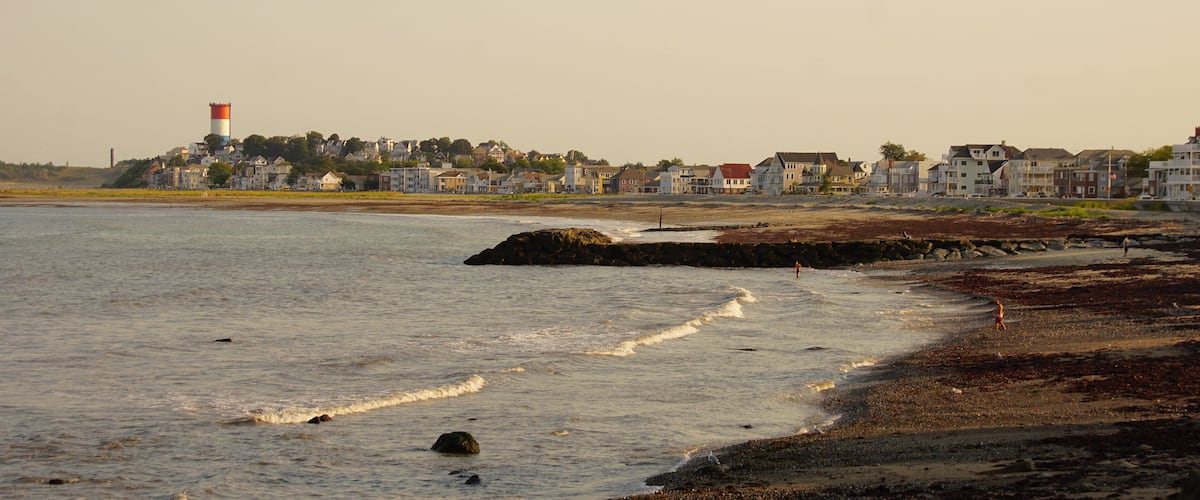 A coastal town with a lighthouse, sandy beach, and residential buildings.