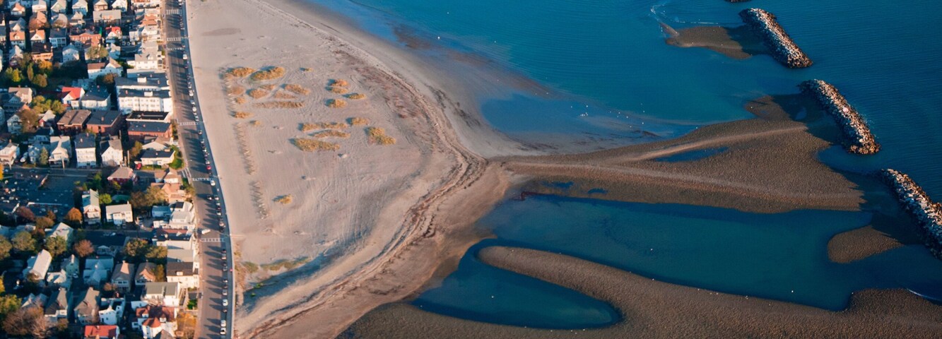 Un pueblo costero con una playa, un muelle y una zona residencial densa.