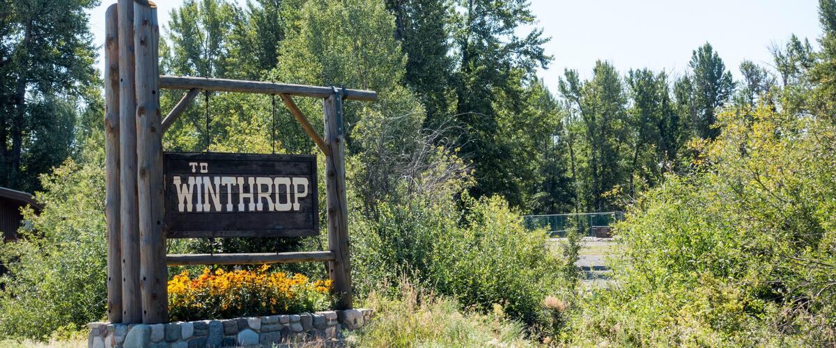 A wooden signpost with 'WINTHROP' written on it, surrounded by greenery and trees.