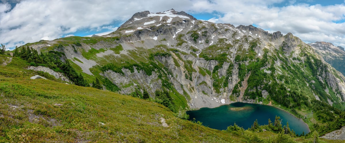A mountain landscape with a lake at its base, surrounded by rocky terrain and patches of greenery.