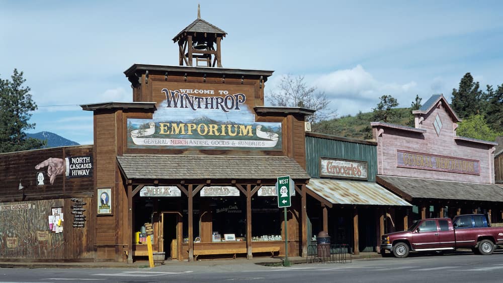 A vintage building with a sign reading "Welcome to Winthrop Emporium" and a vintage car parked outside.