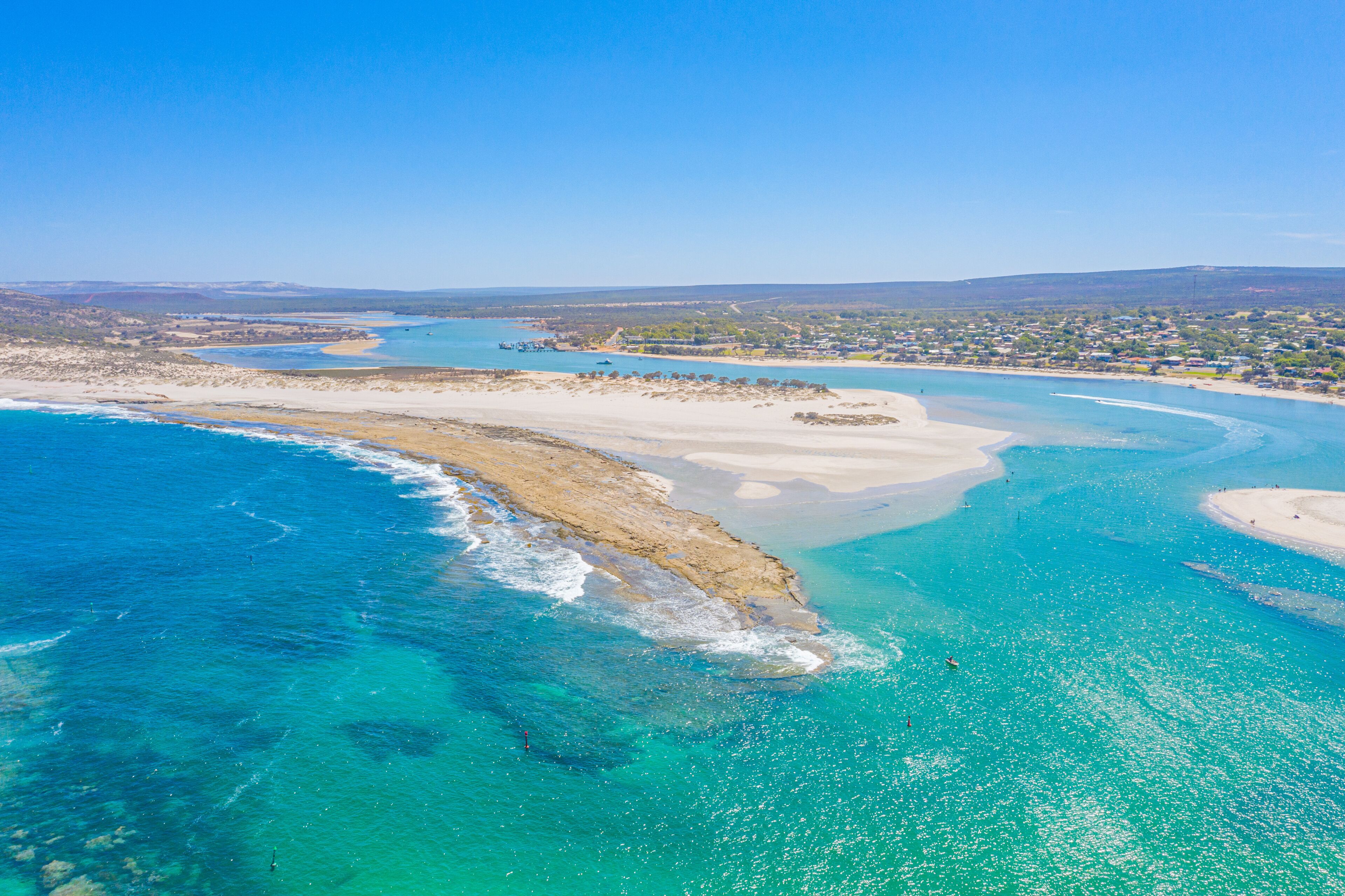 A coastal landscape with clear turquoise waters, sandy beaches, and a distant town.