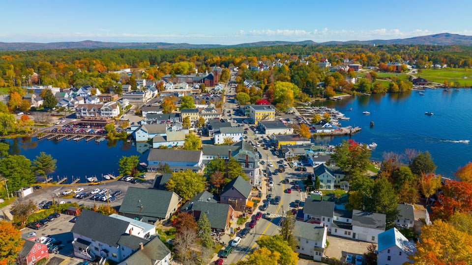 A lakeside town with a marina, autumn foliage, and a distant mountain range.