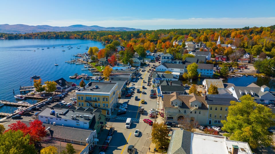 A lakeside town with boats, colorful autumn trees, and a mix of residential and commercial buildings.