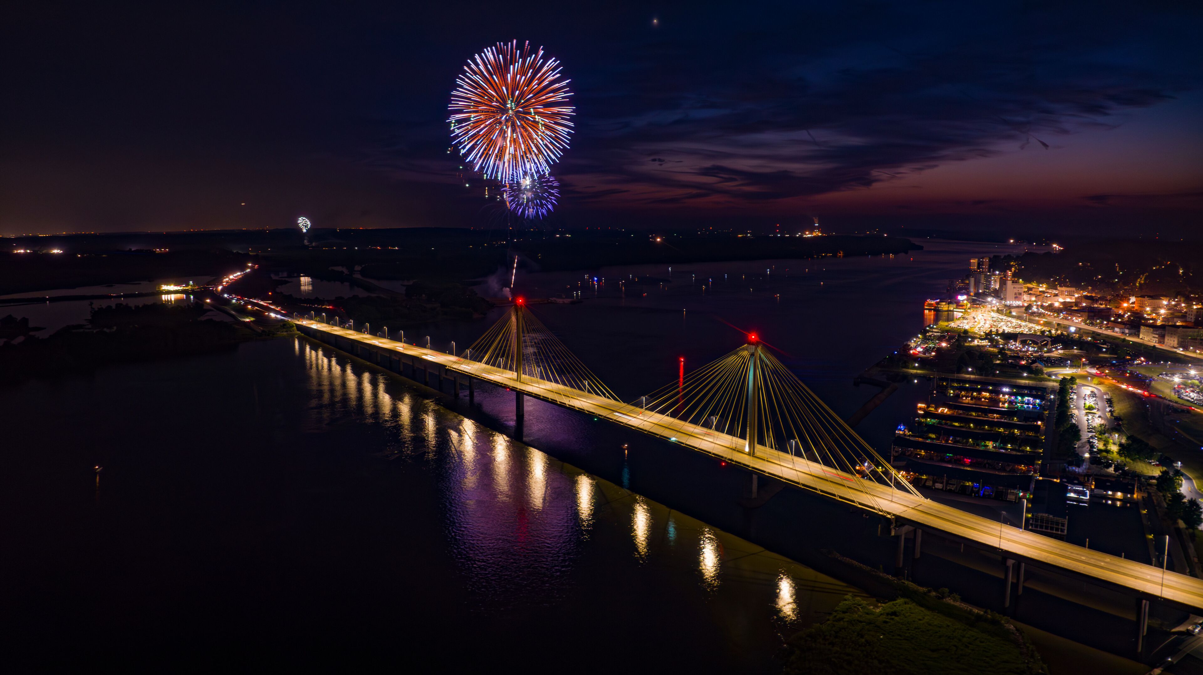 A nighttime view of a bridge with fireworks in the distance.