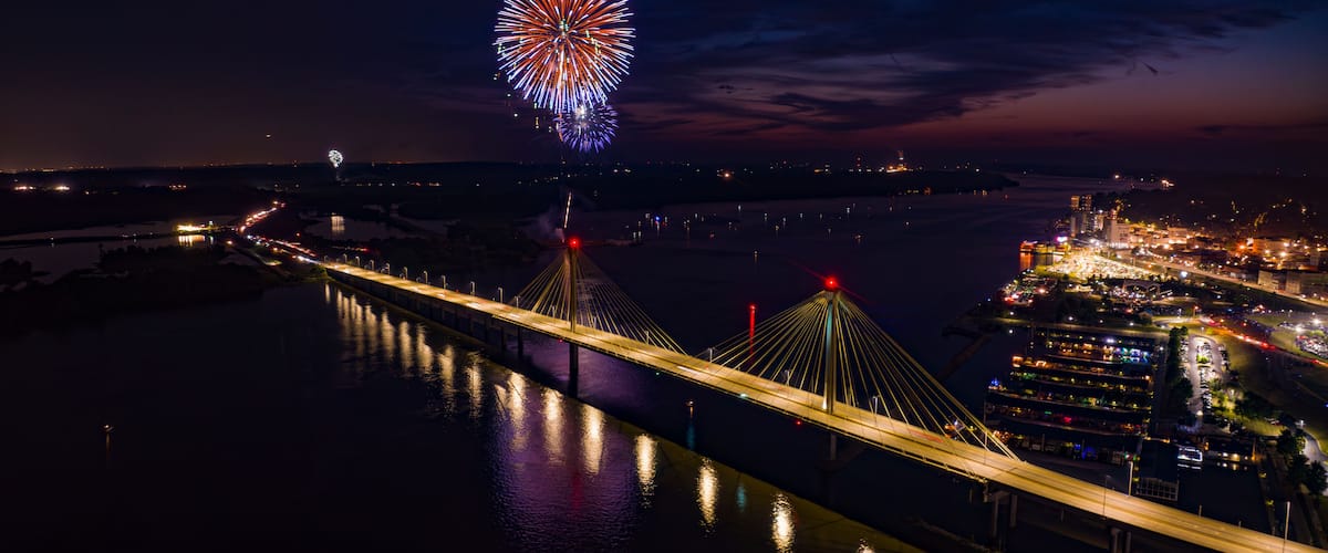 A nighttime view of a bridge with fireworks in the distance.