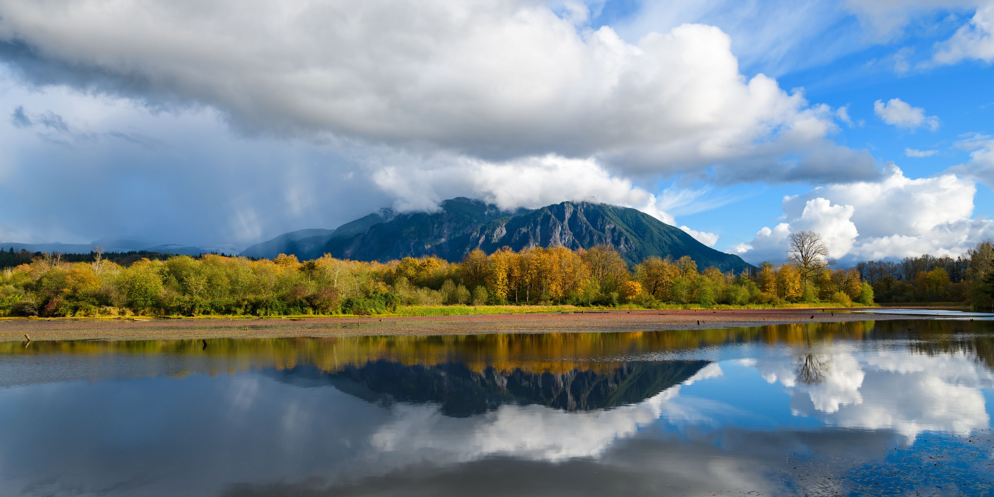 Mount Si reflects in Borst Lake in late fall under partly cloudy sky hanging on the top of the peak in Snoqualmie Washington