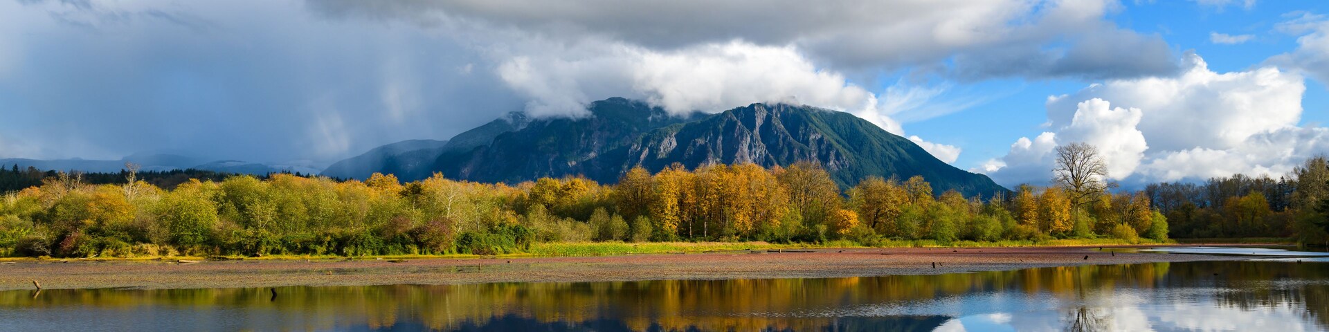 Mount Si reflects in Borst Lake in late fall under partly cloudy sky hanging on the top of the peak in Snoqualmie Washington