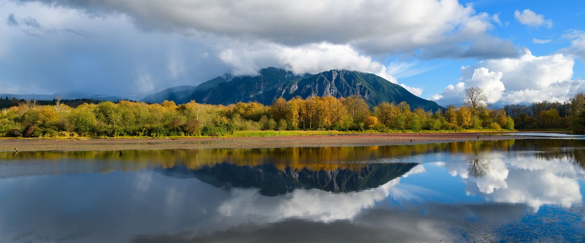 A mountain range, a calm lake, and autumn-colored trees.