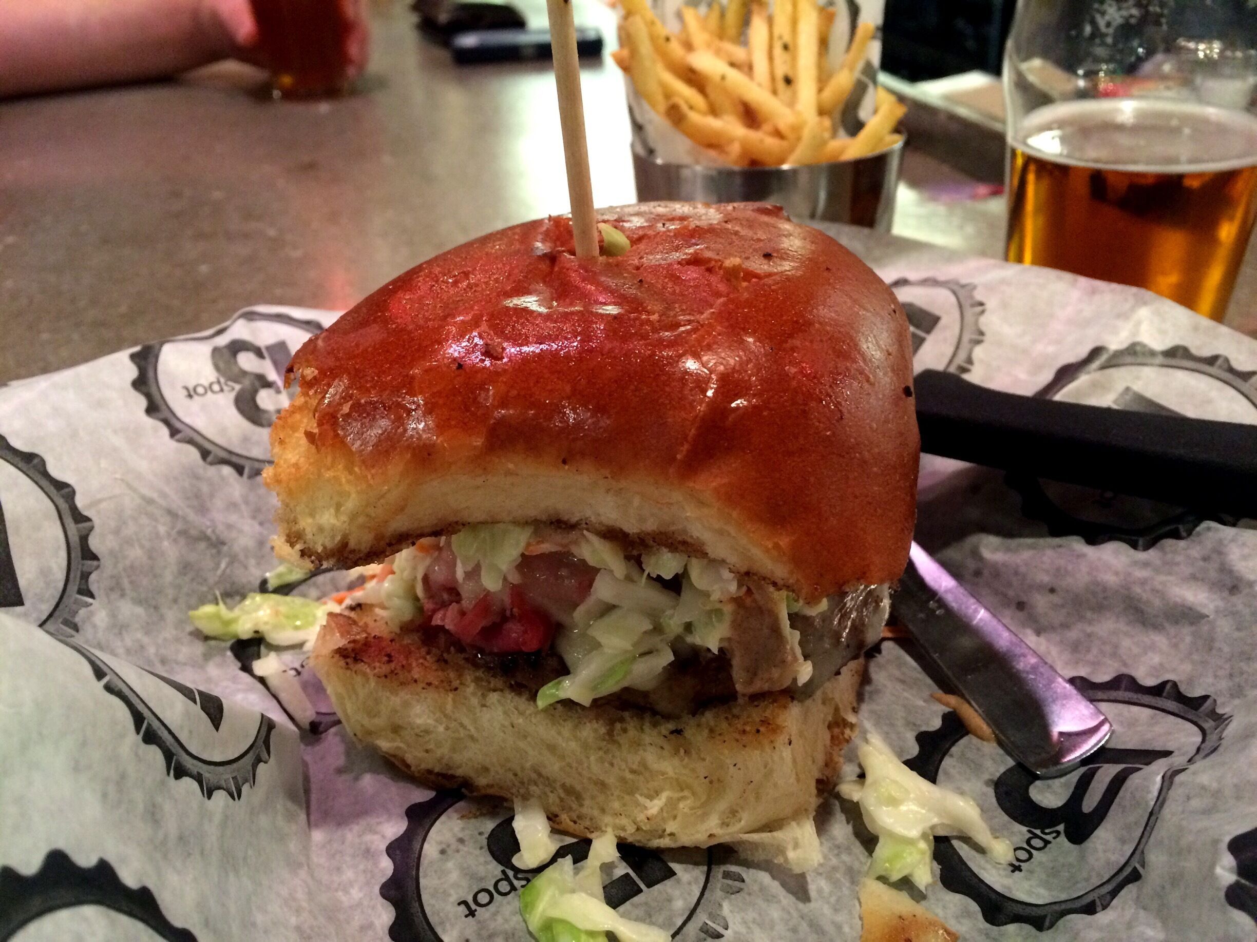 A sandwich with a toothpick, lettuce, and sauce on a paper with a logo.