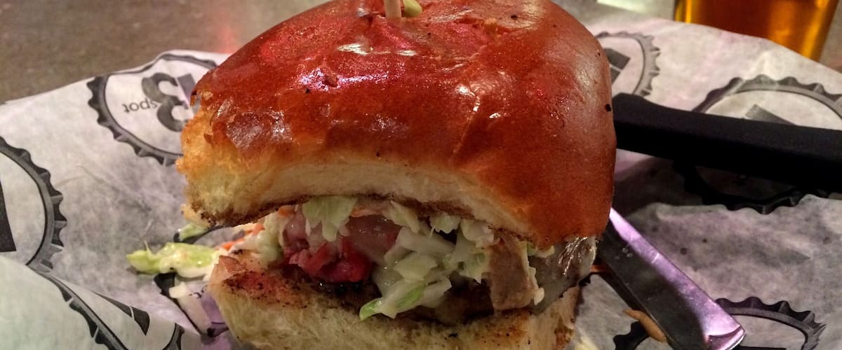 A sandwich with a toothpick, lettuce, and sauce on a paper with a logo.