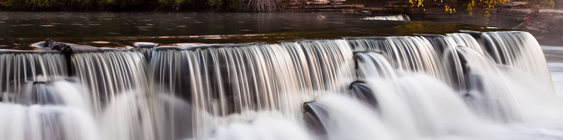 A waterfall with multiple tiers, surrounded by autumn foliage.