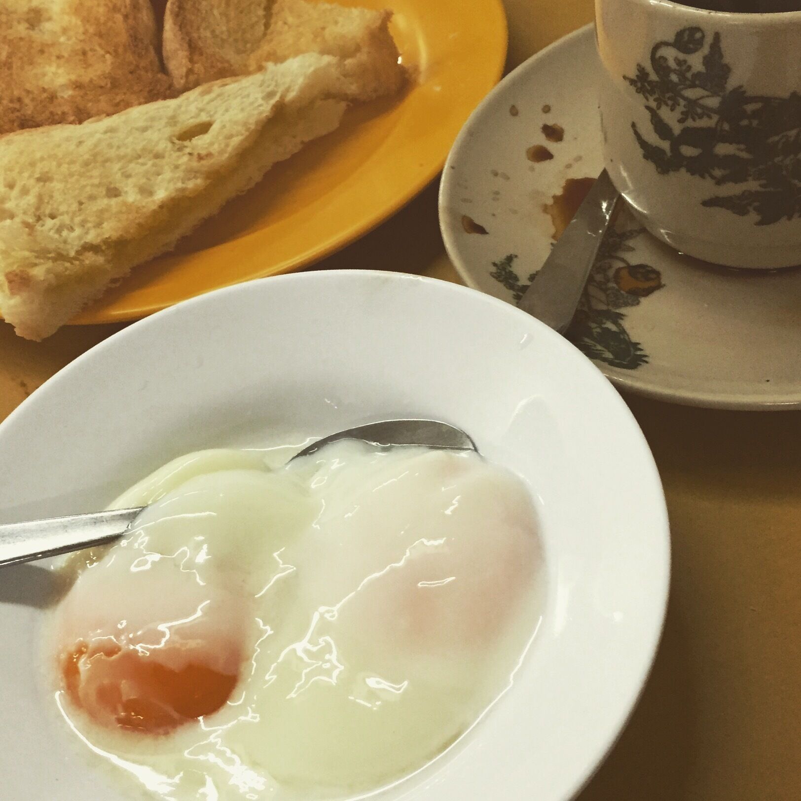 A plate with a poached egg and toast, a cup with floral design, and a knife on a saucer.