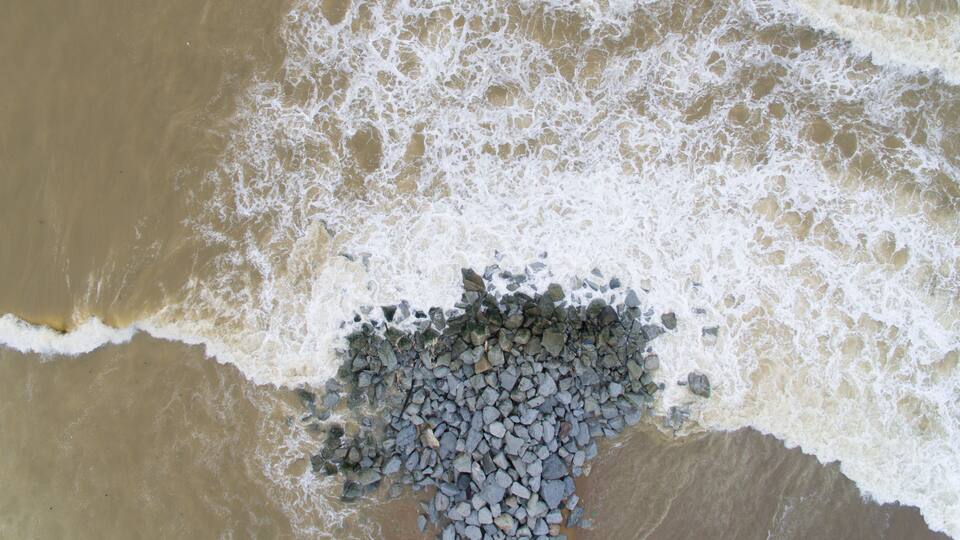 A sandy beach with waves crashing onto a pile of rocks.