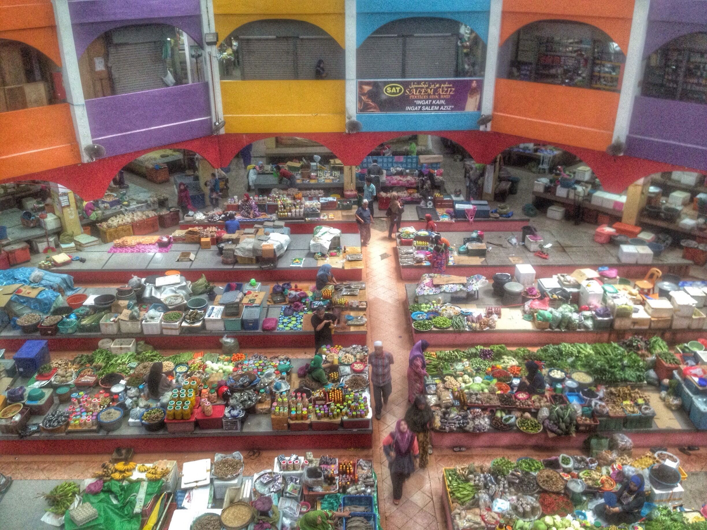 An indoor market with various stalls selling fruits, vegetables, and other goods.
