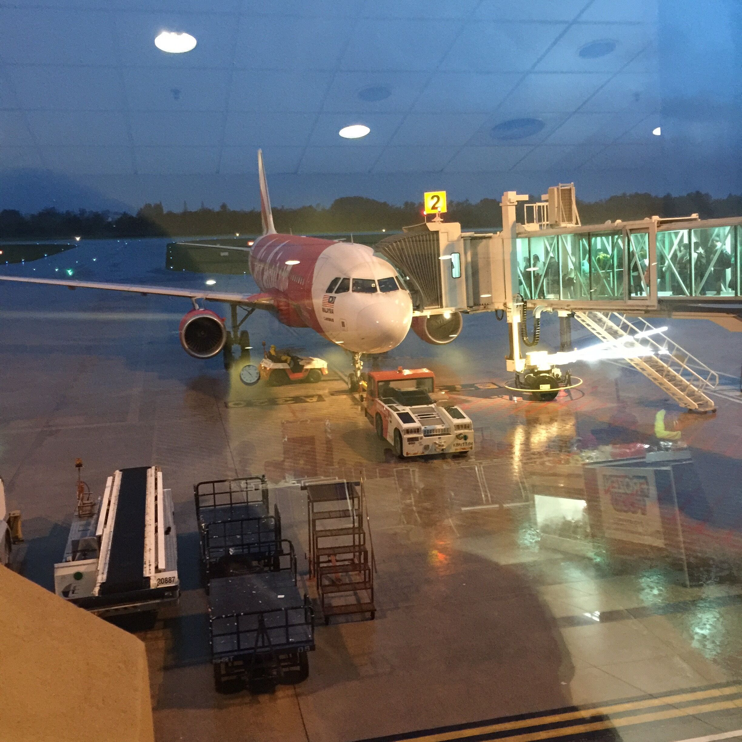 An airplane at a gate with a jet bridge attached, ground support equipment, and a clear sky in the background.