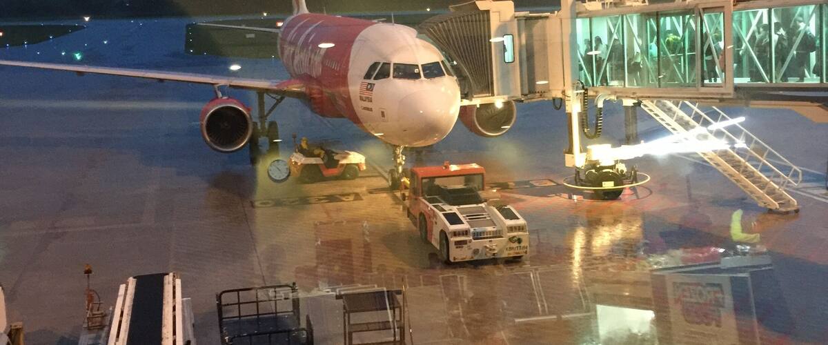 An airplane at a gate with a jet bridge attached, ground support equipment, and a clear sky in the background.