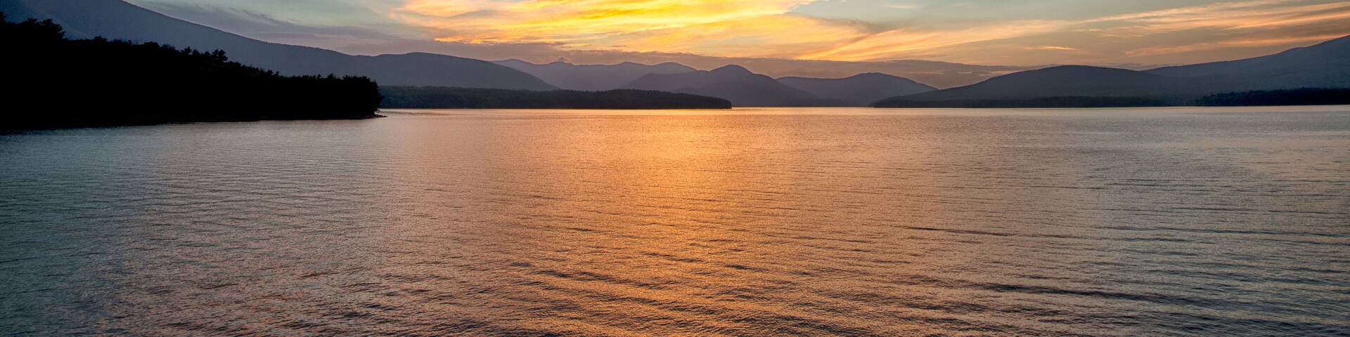 A sunset over a calm lake with mountains in the background.
