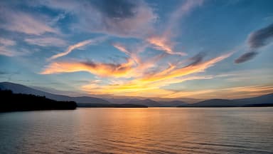 Atardecer sobre un lago tranquilo, con montañas al fondo.