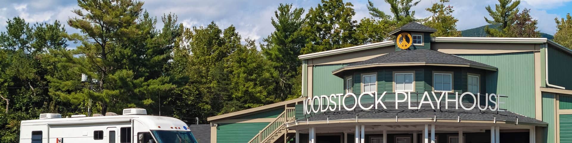 A green building with a sign reading "Woodstock Playhouse" and a white RV parked in front.