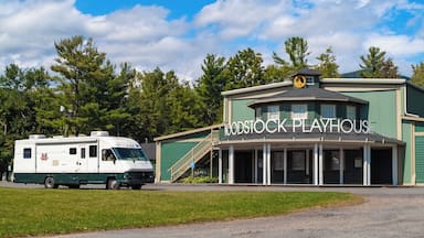 Un edificio verde con un letrero que dice "Woodstock Playhouse" y una caravana blanca estacionada al frente.