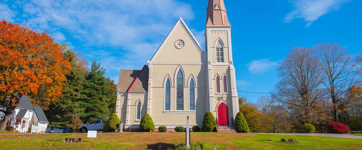 A church with a tall steeple, surrounded by autumn trees and a clear blue sky.