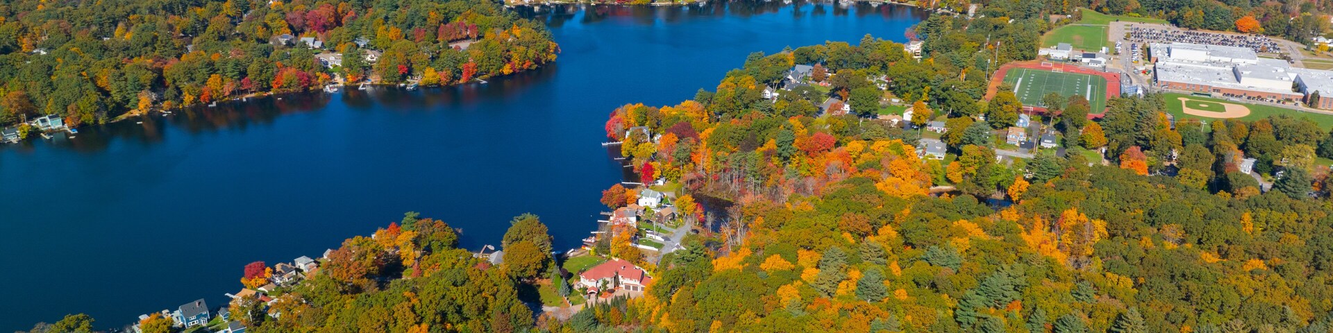 Um lago rodeado por árvores com cores de outono e áreas residenciais.