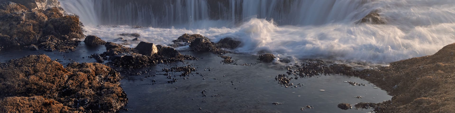 View of Thor's Well with ocean waves crashing into the rocky sinkhole during golden hour along the Pacific coastline in Yachats, Oregon, United States.