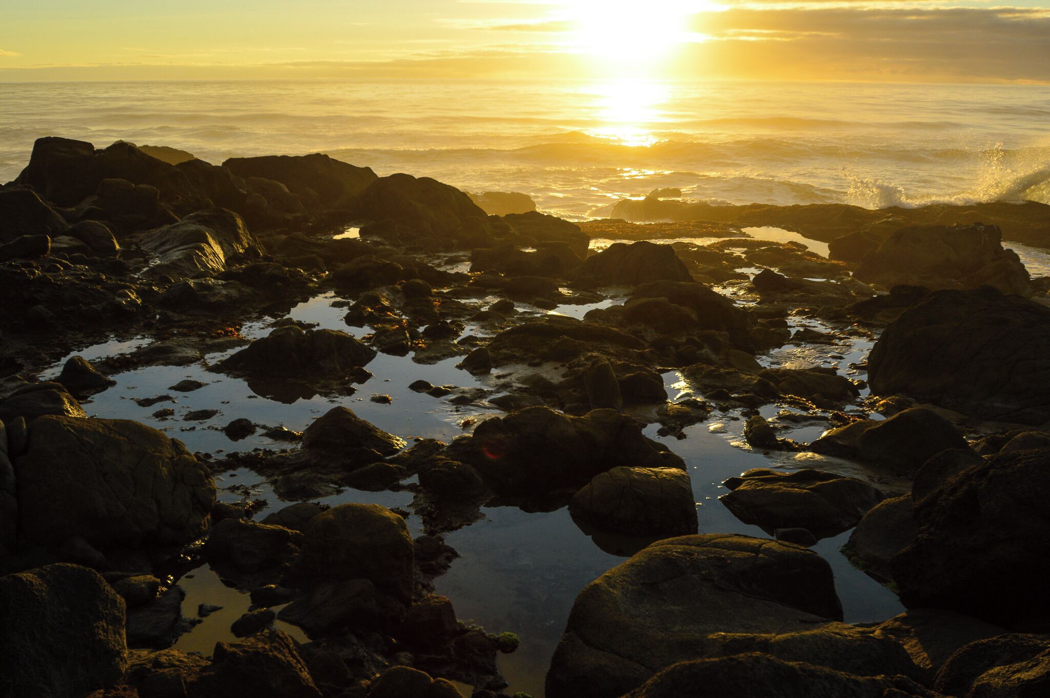 A rocky shoreline with the sun setting over the ocean.