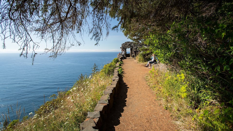 A coastal path with a stone wall, dense greenery, and a clear view of the ocean.