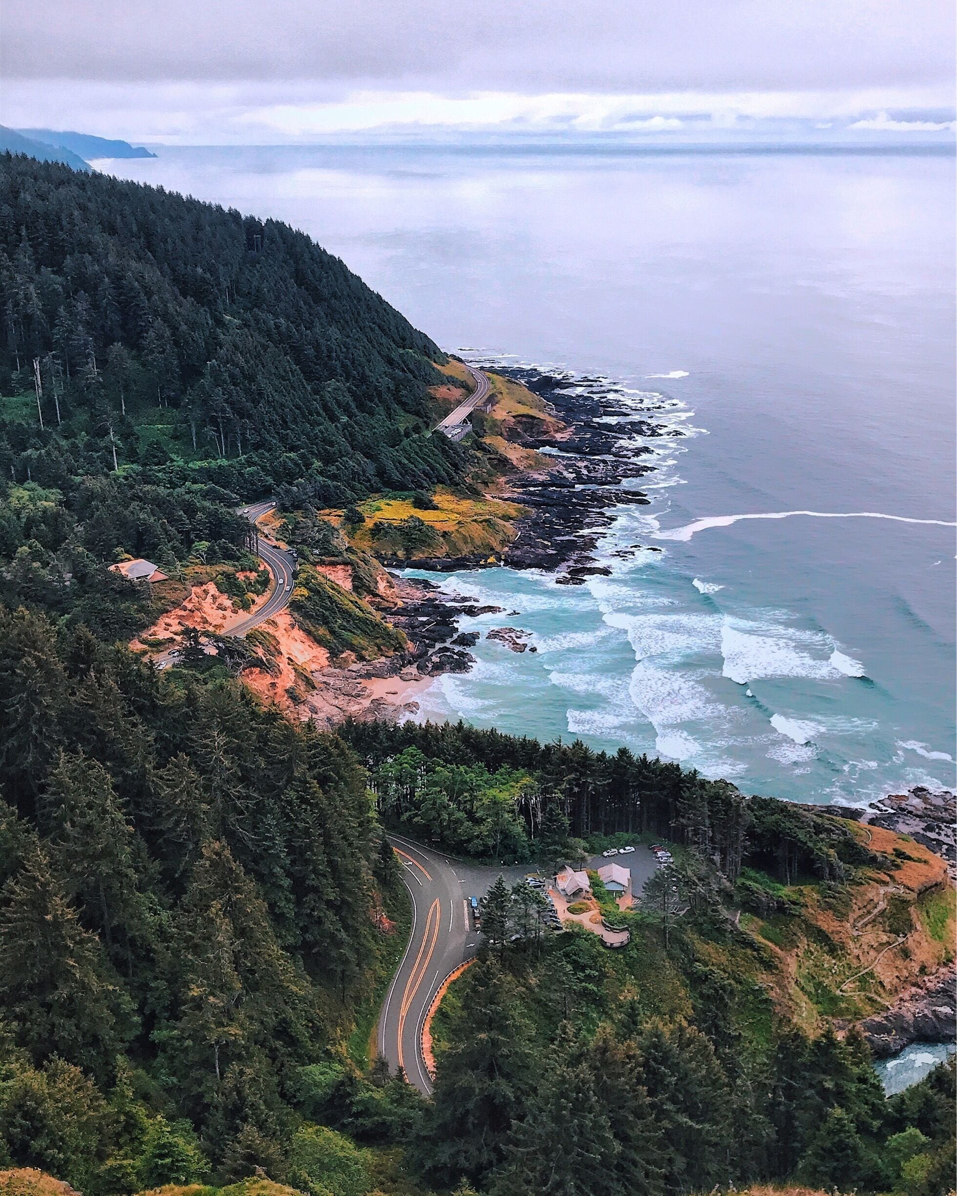 A coastal road winding through a forested area with rocky cliffs and ocean waves.